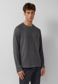 Dark gray long-sleeve sweater with a textured finish, ribbed neckline, and raglan sleeves, paired with dark-colored pants.
