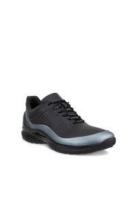 Chaussure de sport noire avec des accents argentés, côtés perforés et lacets noirs brandés, présentée en angle trois quarts sur un fond blanc.
