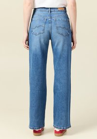 Vaqueros de mezclilla azul claro de pierna ancha con cintura alta, desgastes sutiles, costuras decorativas en los bolsillos traseros y una silueta recta.