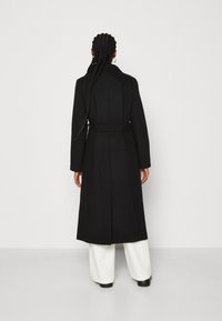 Lungo cappotto nero con vita cintrata, ampi rever e taglio dritto. Presenta una fessura sul retro e una texture del tessuto liscia.