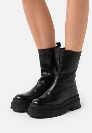 Botas de tobillo de cuero negro con un diseño elegante, punta redondeada, suela de plataforma gruesa y cierre de cremallera lateral con una lengüeta.