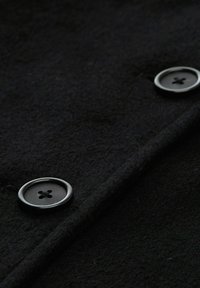 Tessuto di lana nera con una superficie liscia e due pulsanti neri rotondi con un design a quattro fori, cuciti lungo il bordo.