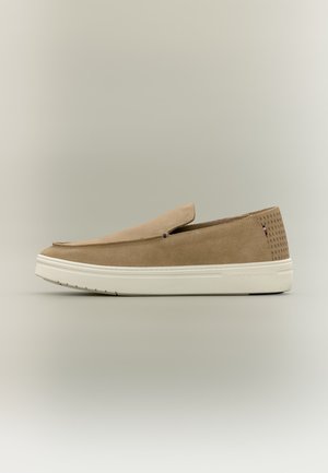 Beige Veloursleder-Slipper-Sneaker mit weißer Gummisohle, perforiertem Fersenbereich und kleinem rot-weiß-blauem Flaggen-Detail an der Seite.