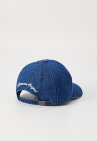 Blue denim cap with a curved visor, adjustable strap at the back, and "American Original" embroidered in white on the side.