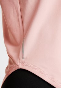 Camiseta atlética de color rosa claro hecha de una tela suave, con una costura lateral que presenta un detalle del logo en gris y un dobladillo redondeado para mayor comodidad.