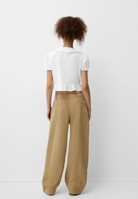 Vit cropped topp med korta puffärmar, volangkrage och nederkant. Kombinerad med avslappnade beiga byxor med vida ben, som har bakfickor.