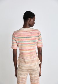 Strukturierter Oberteil und figurbetonter Unterteil mit Zickzackmustern in warmen Farben, darunter Pink, Gelb und Grün, sowie einem Peplum-Detail in der Taille.