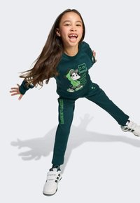 Dark green sweatshirt and pants set featuring a cartoon character, with contrasting light green graphics and white athletic sneakers.