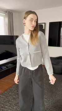 Grå kofta med strukturerat tyg, två framfickor och ribbad nederkant, bärs över en vit topp och kombineras med svarta, löst sittande byxor.