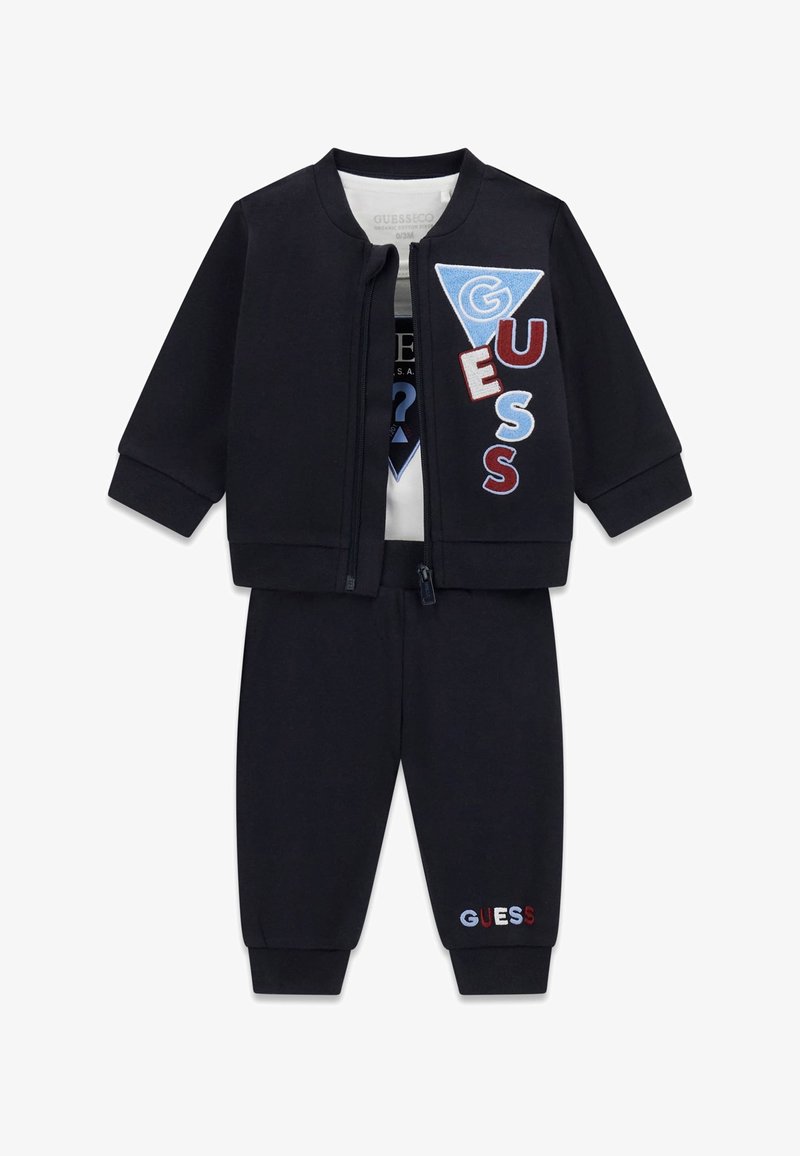 Conjunto negro de tres piezas para niño pequeño con chaqueta con cremallera, camisa blanca y pantalones con parches multicolores con el logo "GUESS".