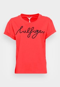 Red cotton t-shirt with short sleeves, round neckline, and curved hem. Features black cursive logo text across the chest.