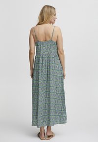 Robe maxi avec un corsage ajusté et une jupe fluide. Présente un motif de feuilles bleues et vertes, des bretelles fines réglables et une texture de tissu douce.