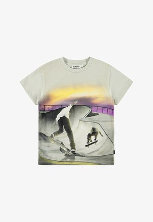 Svetle šedé triko s krátkým rukávem, které zobrazuje grafiku skateboardů v bowl prostředí, s pozadím gradientního západu slunce v purpurových a žlutých odstínech.