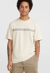 Korte mouw beige t-shirt van katoen, met een zwart patroon over de borst, ronde halslijn en een relaxte pasvorm.