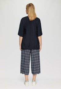 Marineblauw textuurtop met korte mouwen, gecombineerd met geprinte culottes in blauw en crème, aangevuld met zilveren platform sneakers.