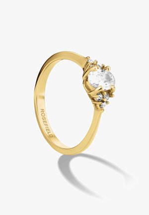 Anillo de oro con una piedra ovalada transparente rodeada de piedras más pequeñas, con una banda elegante y "ROSEFIELD" grabado en el interior.