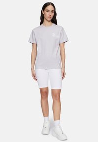 Lyslilla bomulds t-shirt med korte ærmer og hvidt logo tekst, parret med hvide ribbede shorts og hvide sneakers.