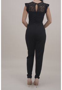 Černý overal s krajkovými detaily na zádech, přiléhavý střih, krátké volánkové rukávy a zúžené nohavice. Nosit s nahými vysokými podpatky.