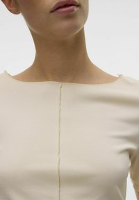 Beige tætsiddende top med firkantet udskæring og struktureret ribbet stof. Synlige sømdetaljer løber vertikalt ned ad midten foran.