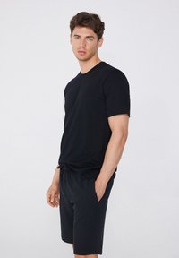 Camiseta negra de manga corta con cuello redondo, combinada con pantalones cortos negros. Ambas prendas tienen una textura suave y un ajuste relajado.