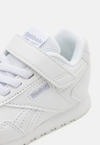 Hvite sneakers laget av syntetisk læder med mesh-detaljer, med en teksturert såle, polstret krage og borrelåsreim. Merkevaren logo vist.