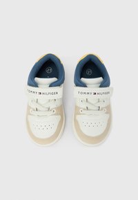 Zapatillas infantiles blancas y beige con cuello acolchado azul, correa ajustable y detalle perforado en la punta. Presenta el logo en la correa.