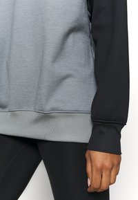 Grå och svart sweatshirt med ribbad ärm och nederkant, med en slät yta och kontrasterande ärmar. Kombinerad med svarta leggings.