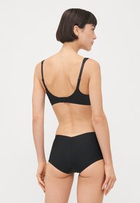 Soutien-gorge noir avec bretelles ajustables et fermeture au dos, associé à des culottes taille haute noires. Texture lisse, design épuré, sans motifs visibles.
