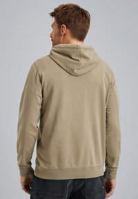 Hoodie beige avec un capuchon à cordon, des manches longues et des poignets côtelés. Tissu lisse et texturé sans motifs ni accents visibles.