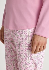Roze langwerpige mouwtop gecombineerd met gestreepte pyjamabroek met bloemmotieven in roze, groen en zwart, die de zachte textuur van de stof benadrukt.