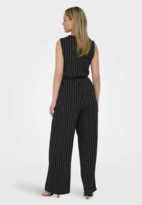 Mono negro a rayas con un diseño sin mangas, piernas anchas, tejido texturizado y cintura con cinturón. Las rayas verticales blancas acentúan el ajuste.