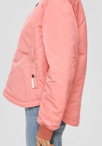 Chaqueta acolchada de color rosa claro con forma cuadrada, bolsillo lateral con cierre a presión, puños acanalados y textura suave.