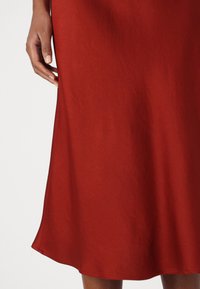 Un vestito rosso fino al ginocchio realizzato in tessuto liscio, leggermente svasato all'orlo, senza motivi visibili o dettagli in metallo.
