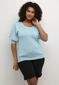 Maglione corto blu chiaro a maniche corte con scollo a barca e maniche a palloncino, abbinato a pantaloni corti neri arrotolati. Tessuto a maglia testurizzato.