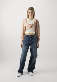 Light pink sheer blouse with ruffled edges, white fitted top underneath, paired with loose blue jeans featuring visible distressing and white sneakers.