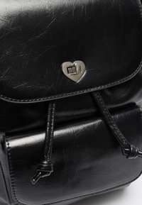 Black leather backpack with a heart-shaped silver clasp and adjustable leather drawstrings on the front pocket.