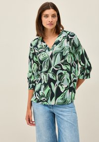 Blouse à imprimé floral dans des nuances de vert sur fond noir, présentant un décolleté en V, des manches trois-quarts et des poignets texturés.