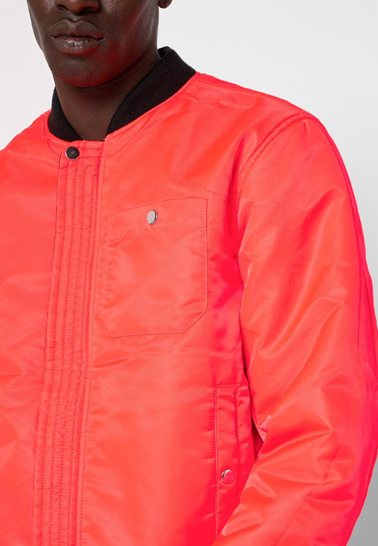 Veste bomber en néon rose en tissu glossy, avec un col côtelé, une poche à pression sur la poitrine et des accents en métal.