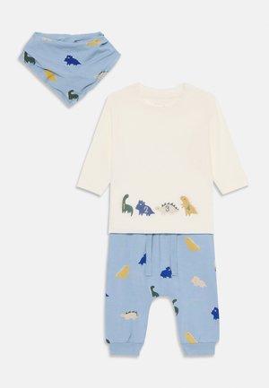 Dreiteiliges Kinderoutfit mit einem weißen Langarmshirt mit bunten Dinosaurierdrucken, blauen Hosen mit ähnlichen Mustern und einer passenden Schürze.