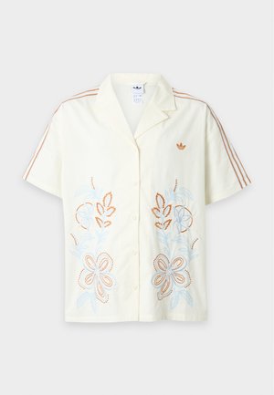 Chemise crème à manches courtes avec fermeture boutonnée devant, motifs floraux brodés orange, trois bandes orange sur les manches et petit logo sur la poitrine.