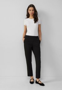 Haut blanc côtelé à manches courtes avec des bords festonnés, associé à un pantalon noir ajusté et des ballerines noires à bout pointu, créant une silhouette élégante.