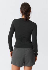 Top negru cu mânecă lungă, cu o textură netedă, asortat cu pantaloni scurți gri. Ținuta are un design ajustat și o croială simplă.