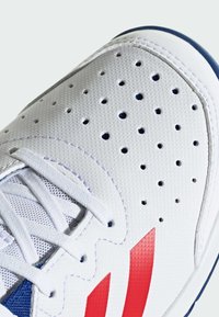 Chaussure de sport blanche avec tige en mesh, perforations pour la respirabilité, accents en bleu, bandes rouges et lacets blancs. Semelle en caoutchouc.