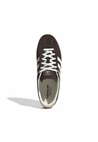 Καφέ σουέντ αθλητικό παπούτσι με λευκές ρίγες, λευκά κορδόνια και ελαστική σόλα. Διαθέτει υφασμένη γλώσσα και εσωτερική σόλα με λογότυπο.