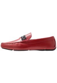 Rote Lederloafers mit glatter Textur, einem rechteckigen Zungen-Detail und einem schwarzen Etikett auf dem Obermaterial. Flache Sohle mit sanfter Kurve.