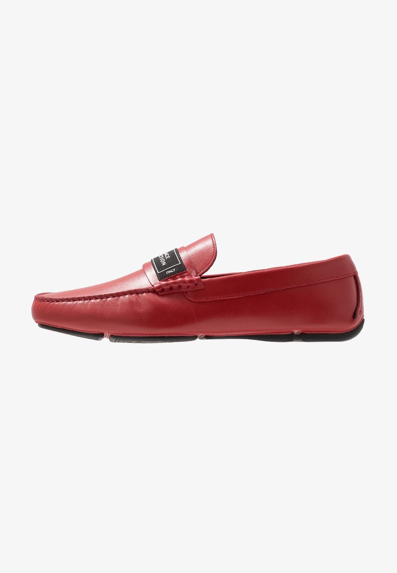 Rote Lederloafers mit glatter Textur, einem rechteckigen Zungen-Detail und einem schwarzen Etikett auf dem Obermaterial. Flache Sohle mit sanfter Kurve.