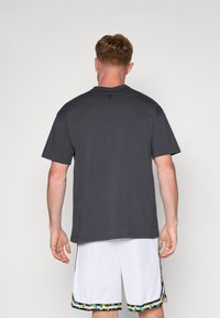 Grå bomuld t-shirt med rund halsudskæring, korte ærmer og et logoaccent. Båret sammen med hvide basketballshorts med en flerfarvet mønstret kant.
