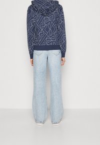 Felpa navy con motivi geometrici bianchi e cappuccio con cordino, abbinata a jeans ampi azzurri con orlo sfrangiato.