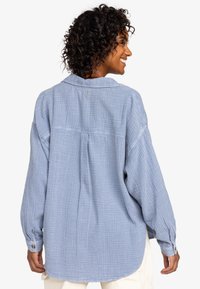 Light blue, textured long-sleeve shirt with a loose fit, button-down collar, and a pleat at the back; features button cuffs and a soft fabric.