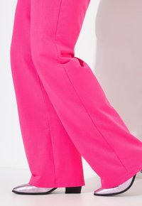 Pantalons larges rose vif en tissu lisse, associés à des chaussures à talons argentées brillantes. Lignes épurées et design moderne.